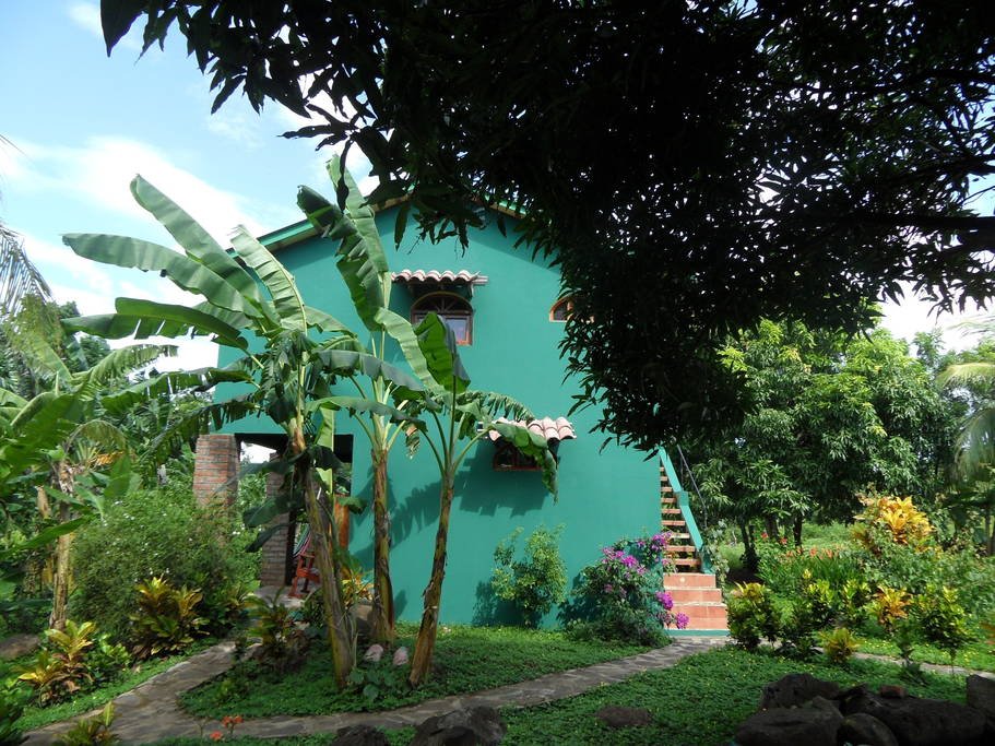 แบบบ้านปูนสองชั้น ทาผนังสีเขียว มีสวนต้นไม้และพืชผักรอบบ้าน
